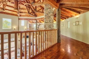 A spacious interior with wooden beams, a stone pillar, and a balcony with a railing.