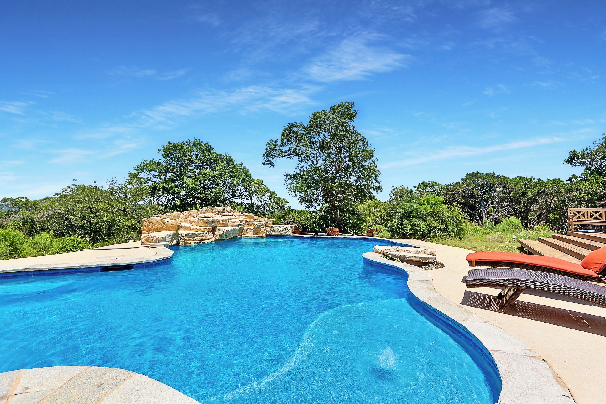 Una piscina azul cristalina de borde curvo, rodeada de sillones de descanso y una formación rocosa de piedra.