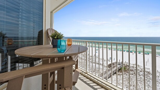 A balcony with a wooden table, a potted plant, and a view of the beach and ocean. - Gulf Dunes 617: Sand Dollar Daze - Marvelous 3 bed, 3 bath unit! A must see! (Fort Walton Beach)