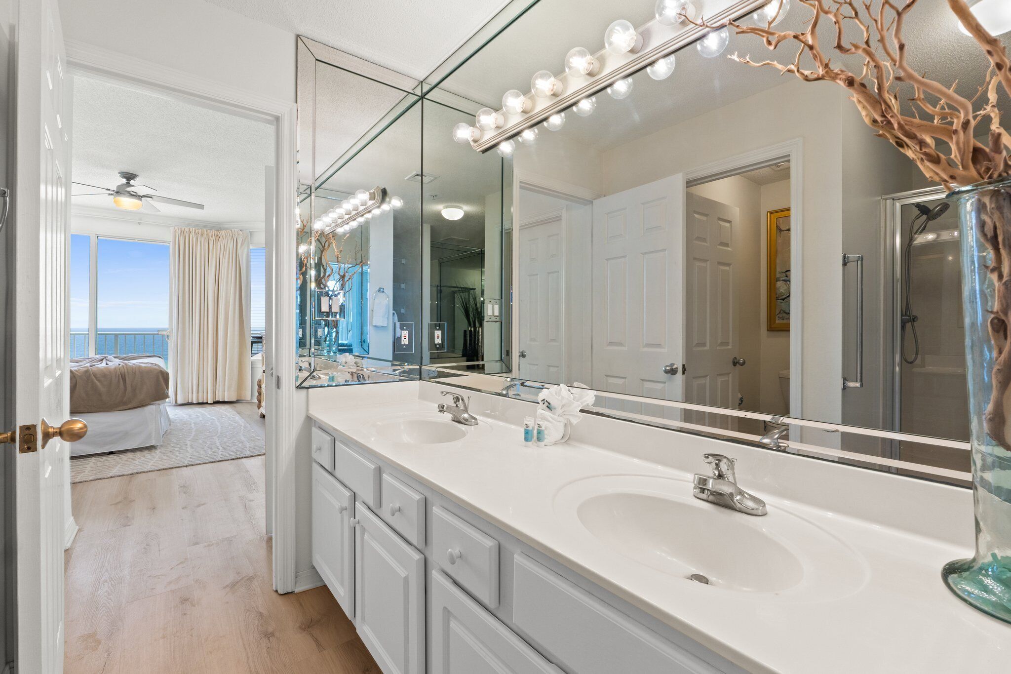 A bathroom with a large vanity mirror, two sinks, and a ceiling fan.