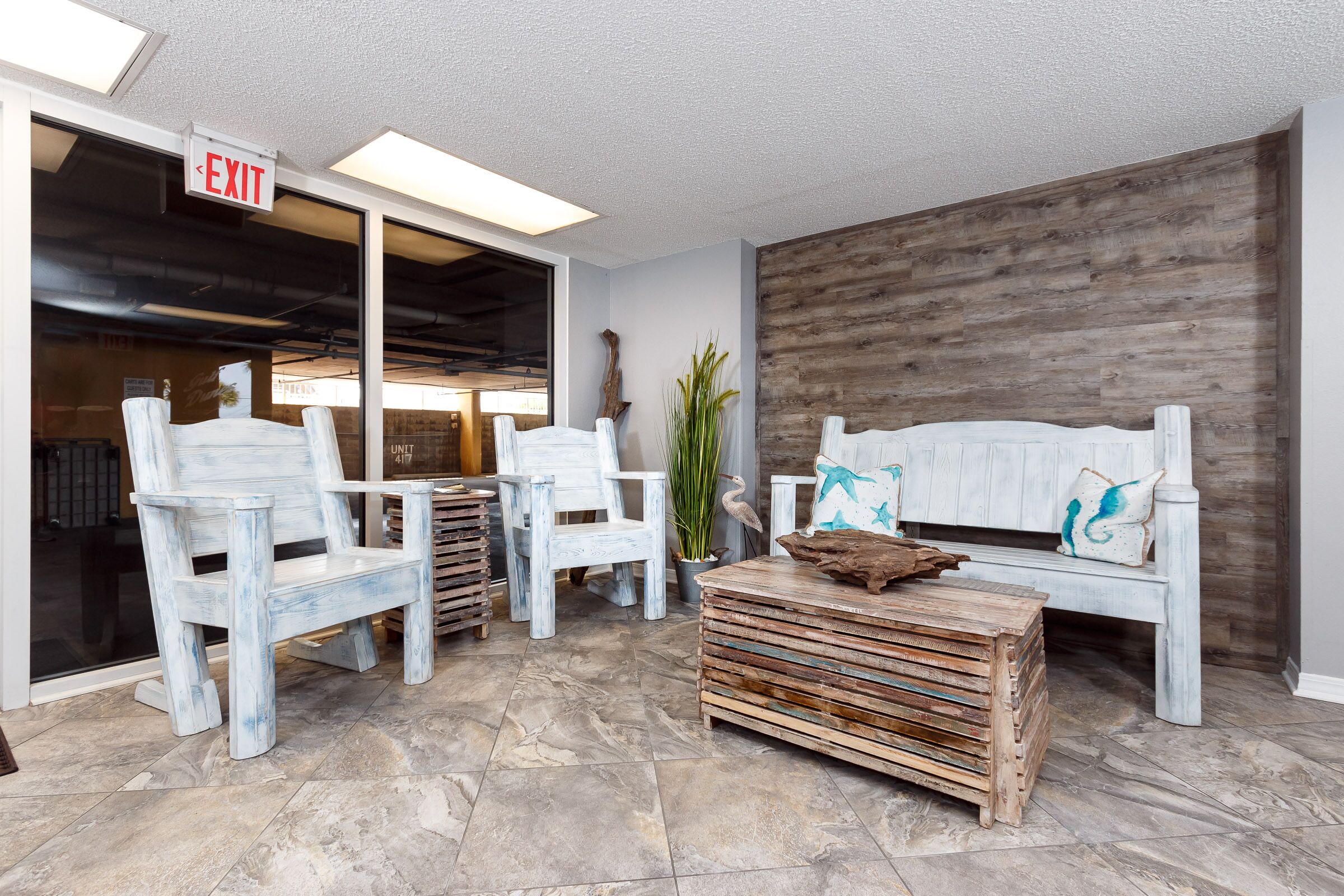 A lobby with white chairs and a wooden bench, an exit sign, and a wooden wall.
