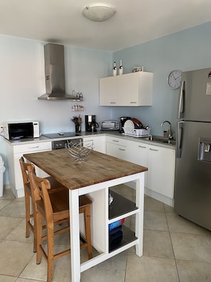 A compact kitchen with white cabinets, a wooden table, and a stainless steel refrigerator.