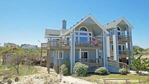 A large, multi-story house with a balcony and a flag. - OH1200- 5 BRs with 2 Masters, Private Pool, Hot Tub, Foosball and Volleyball! (Corolla)