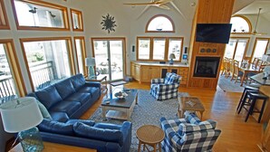A spacious living area with a blue sofa, a checkered armchair, a coffee table, and a fireplace. - OH1200- 5 BRs with 2 Masters, Private Pool, Hot Tub, Foosball and Volleyball! (Corolla)