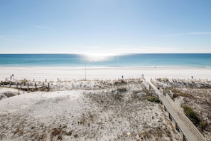 A beach with a wooden boardwalk leading to the water, sandy dunes, and a clear sky.