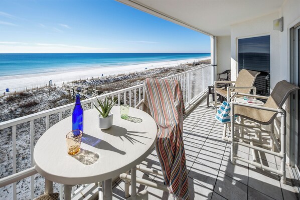A balcony with a view of the beach, a table with a bottle and glass, and a chair.