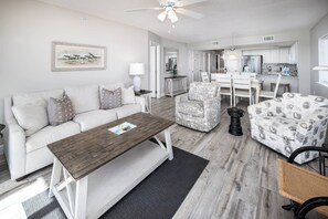 A modern living room with a sofa, coffee table, patterned armchairs, and a dining area with chairs and a table.