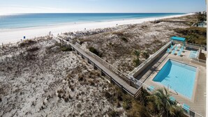 Blick auf einen Strand mit einem hölzernen Steg, der zu einem Poolbereich führt.
