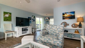A living room with a TV, a patterned sofa, a white chair, and a ceiling fan.