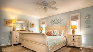 A bedroom with a bed, nightstands, a ceiling fan, and decorative wall art.
