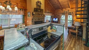 Una acogedora cocina de estilo rústico con chimenea de piedra, una estufa grande y un comedor con sillas de madera.
