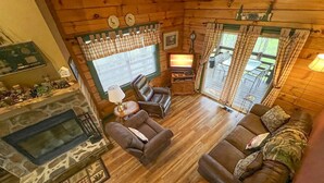 Interior acogedor de una cabaña con chimenea, sofás de cuero y una televisión.