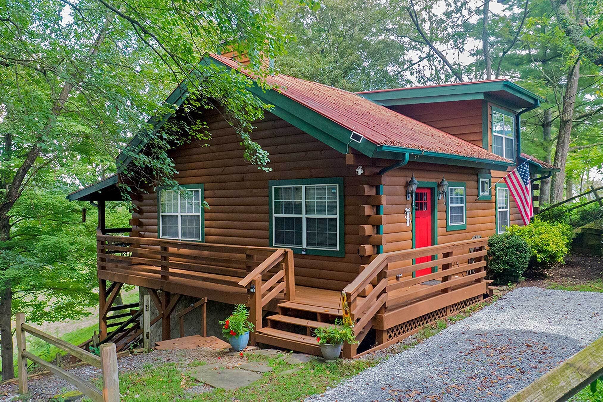 A rustic log cabin with a red door, wooden steps, and a small porch area.
