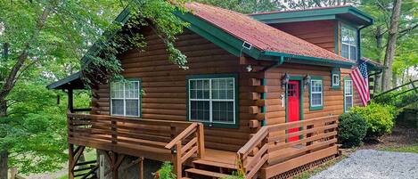 A rustic log cabin with a red door, wooden steps, and a small porch area.