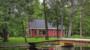 A red house with a pond in front, surrounded by trees. - Secluded Birnamwood Cottage w/ Deck & River Views! (Birnamwood)