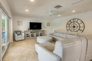 Una sala de estar con un sofá, un reposapiés y un sillón, un televisor y un reloj de pared.