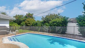 Una piscina con bordo piastrellato, una recinzione e una casa sullo sfondo.