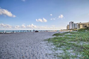 Una playa con arena, sombrillas y algunos edificios al fondo.