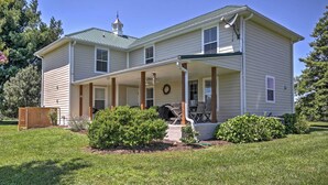 A two-story house with a covered porch, a chimney, and a small garden area with bushes and a lawn. - 'Anny's Farm House' Near Middleburg & Wineries! (Round Hill)