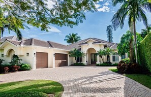 A two-story house with a paved driveway, a garage, and a well-maintained lawn. - SOUTHERN SUNSET - Olde Naples, Heated Pool & Spa, Walk to the beach! (Naples)