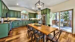 Una cocina amplia con gabinetes verdes, una mesa de comedor de madera y un ventanal con vistas a una terraza.