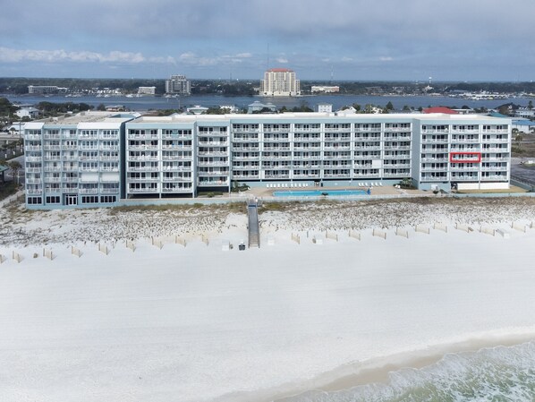 A beachfront hotel with multiple balconies, a swimming pool, and a beach in the foreground.