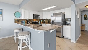 Cocina moderna con armarios blancos, una isla central con taburetes, electrodomésticos de acero inoxidable y un reloj en la pared.