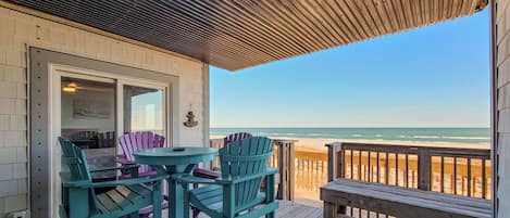 A wooden deck with a table and chairs, overlooking a beach.