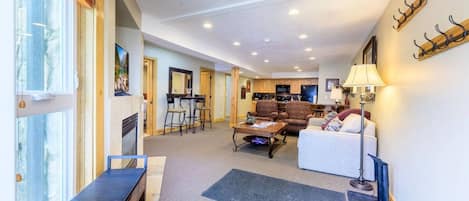 A spacious living area with a sofa, a coffee table, and a bench. There is a kitchen area in the background with a dining table and chairs.