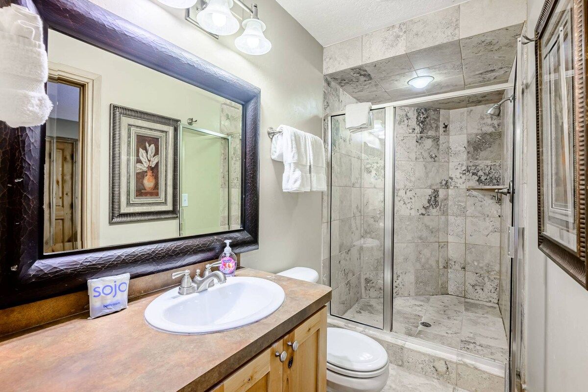 A bathroom with a large mirror, a sink, a toilet, and a glass-enclosed shower.