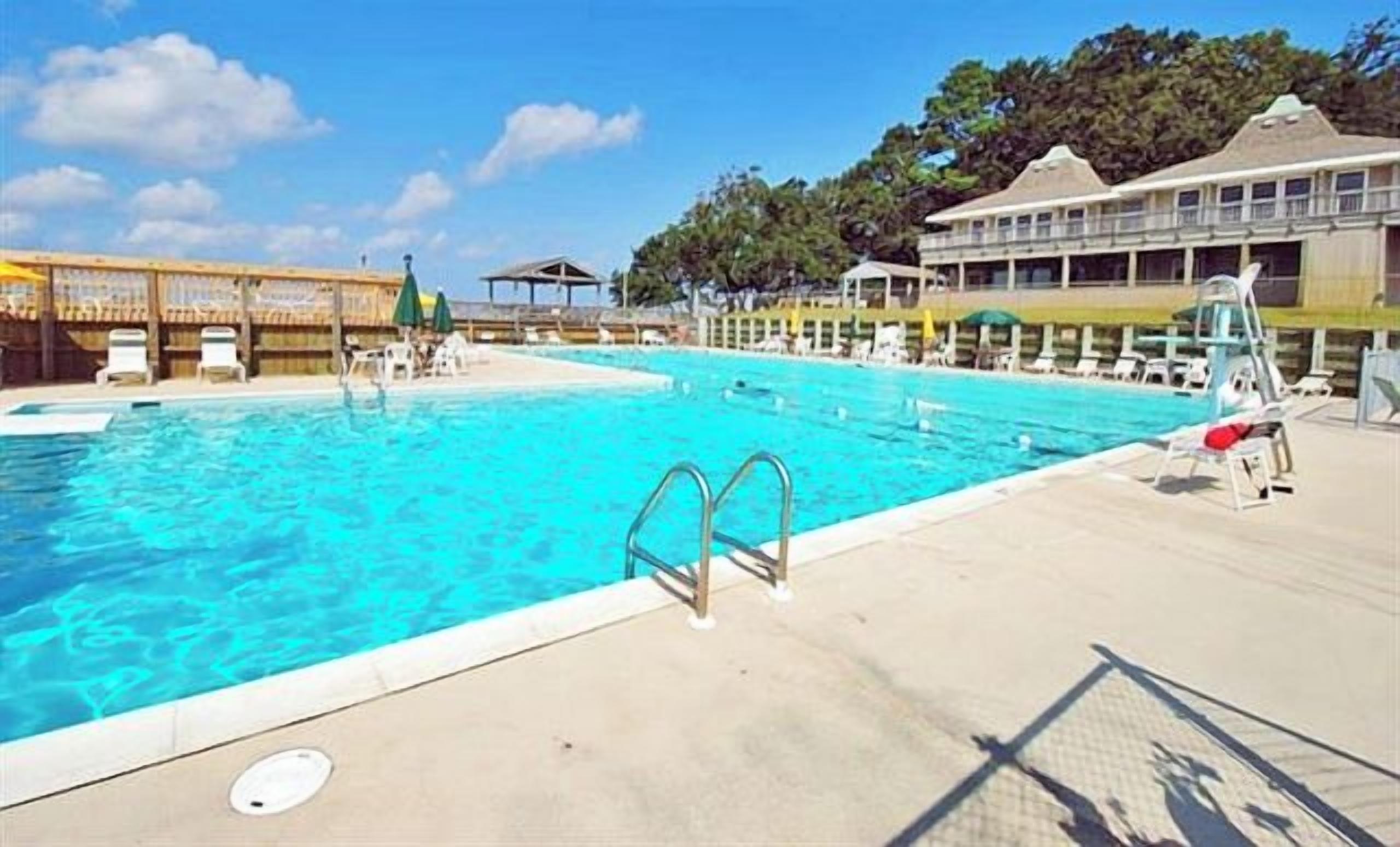 A community pool with clear blue water, a lifeguard tower, and lounge chairs along the poolside.
