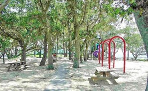 Un parc équipé de tables de pique-nique, de bancs et d’aires de jeux pour enfants.