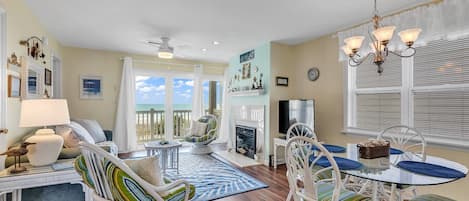 A spacious living room with a balcony, a fireplace, and a dining area with white wicker furniture.