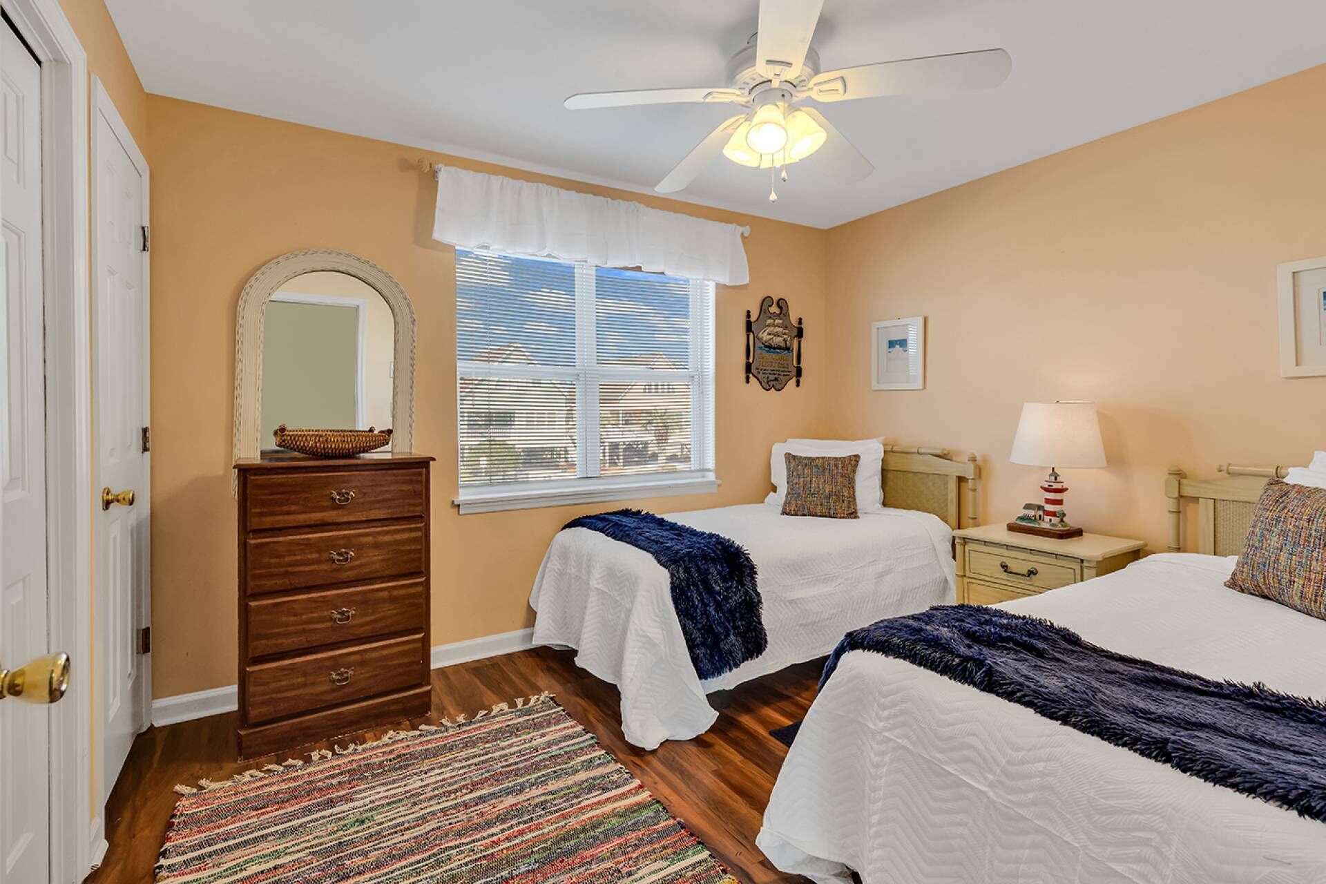A bedroom with two beds, a dresser, a ceiling fan, a window with blinds, and a rug.
