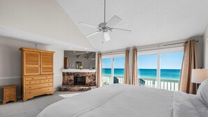 Une chambre dotée d’un grand lit, d’une armoire en bois, d’une cheminée en pierre et offrant une vue sur l’océan grâce à de grandes fenêtres.