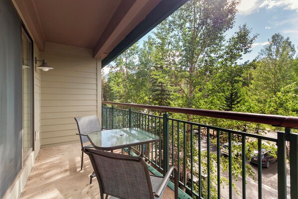 A balcony with a glass table and chairs, a view of trees, and a parked car in the background. - Extremely convenient ski-in/ski-out, Quick walk to downtown Breckenridge, Privat (Breckenridge)