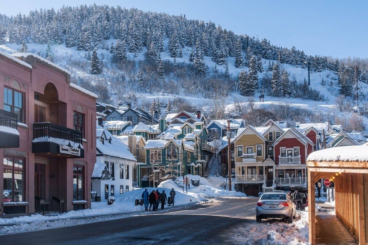 A snow-covered street with buildings, a stop sign, and a car.