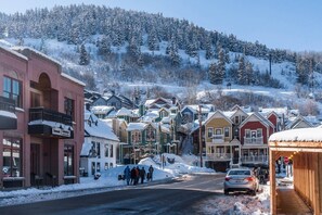 A snow-covered street with buildings, a stop sign, and a car.