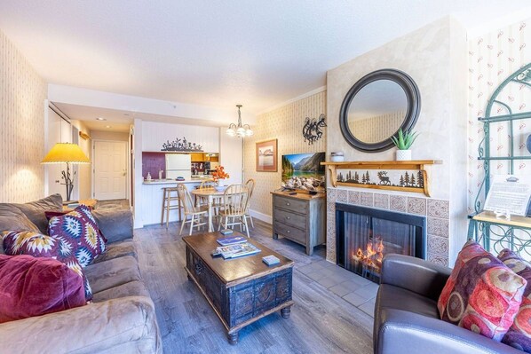 A living room with a fireplace, a dining area, and a kitchen in the background.