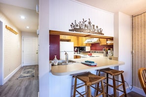 A kitchen with a central island, wooden stools, and a decorative wall piece.