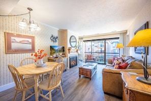 A cozy living room with a fireplace, a dining area with wooden furniture, and a large window offering a view of the outside.