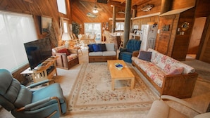 A cozy cabin interior with a wooden ceiling, a fireplace, a dining area, and a living room furnished with sofas and chairs. - WH1091- Oceanfront-  6 BRs, Cargo Lift, Great Ocean Views Dog Friendly! (Corolla)