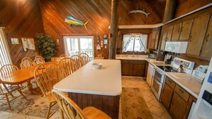 A wooden cabin interior with a dining area, kitchen, and a large window. - WH1091- Oceanfront-  6 BRs, Cargo Lift, Great Ocean Views Dog Friendly! (Corolla)
