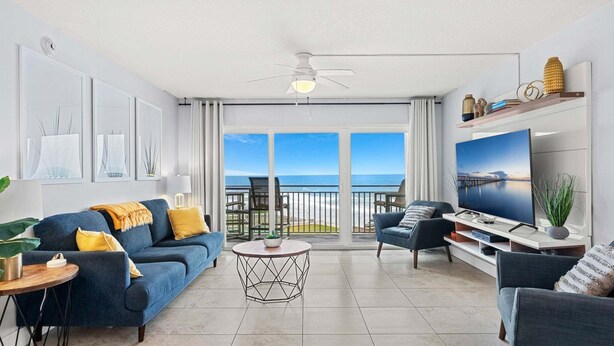 Een woonkamer met een bank, fauteuils, een salontafel, een televisie en een balkon met uitzicht op de oceaan.