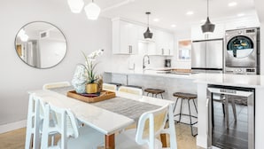 Een moderne keuken met witte kasten, een centraal eiland, roestvrijstalen apparatuur en hanglampen.