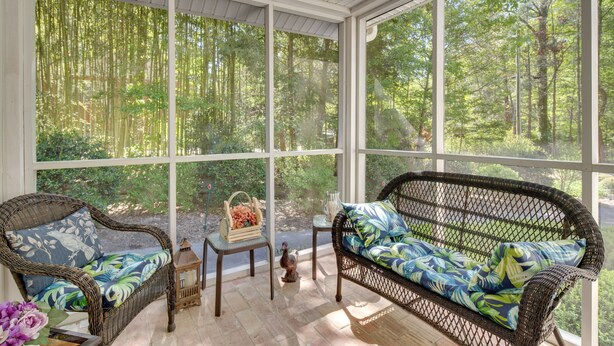 A sunroom with wicker furniture and large windows overlooking a forest. - 7 Mi to the Biltmore: 'Le Canard' Cottage w/ Porch (Arden)