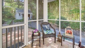 A covered porch with a wicker chair, a small table with a vase of flowers, and a lantern. - 7 Mi to the Biltmore: 'Le Canard' Cottage w/ Porch (Arden)