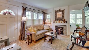 A cozy living room with a sofa, coffee table, and fireplace. There is a door with a window, a mirror, and a television. - 7 Mi to the Biltmore: 'Le Canard' Cottage w/ Porch (Arden)