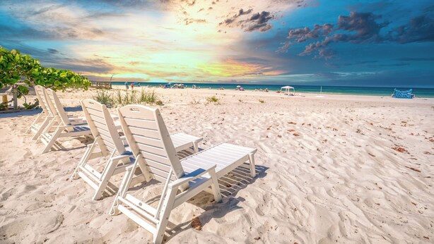 A beach with white lounge chairs and a wooden pier in the background.