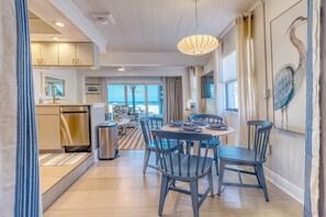 A modern kitchen with a dining area, featuring a large window with a view of the beach.